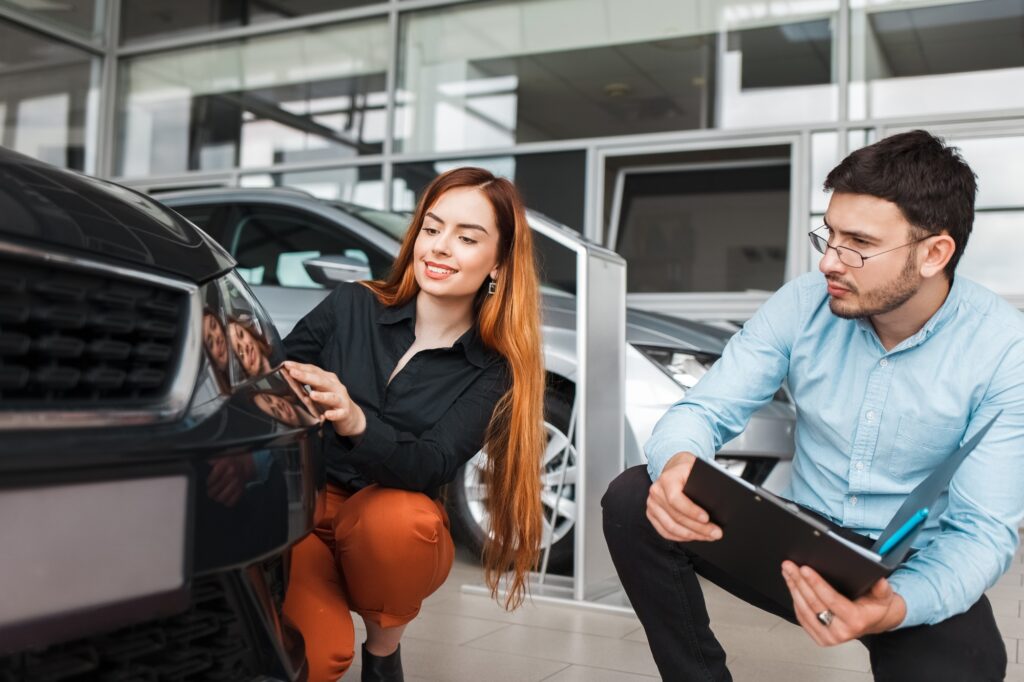 Salesman shows the car to a young client of a car dealership. Girl chooses a new car